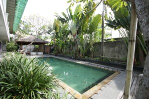 Una piscina rodeada de exuberante vegetación y un quiosco tradicional.