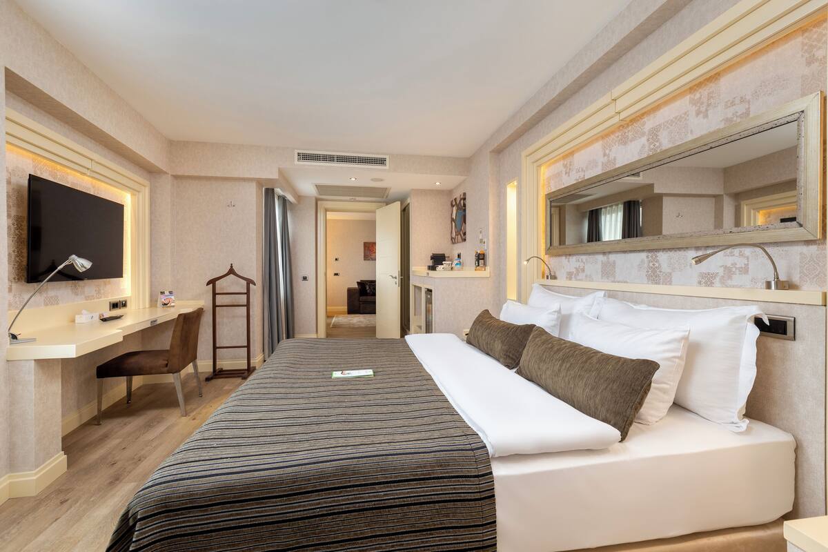 Een hotelkamer met een bed, een bureau, een stoel, een televisie en een grote spiegel.