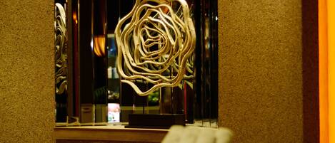 Una habitación con una escultura metálica decorativa, un escritorio de madera y una ventana con cortinas.