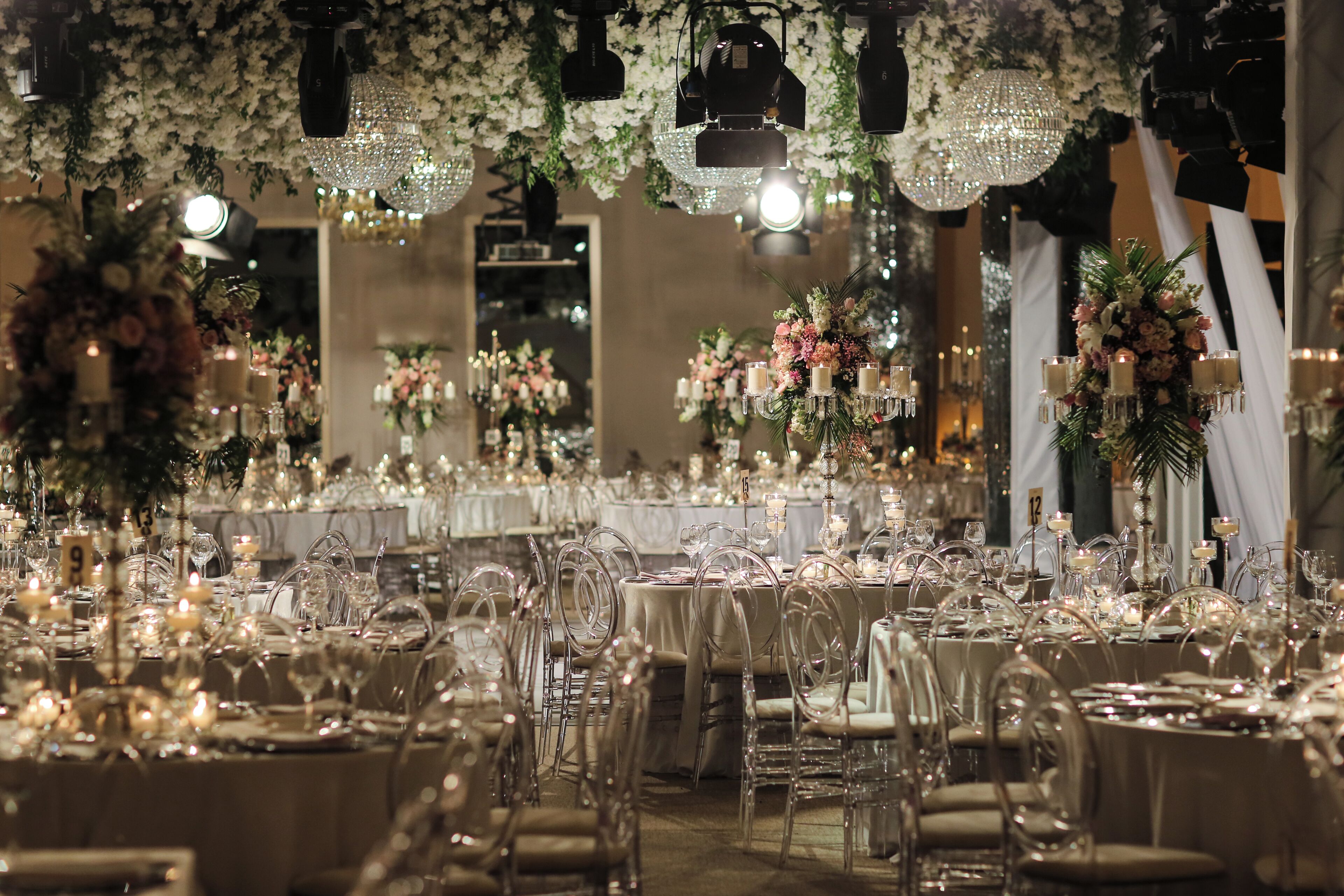 A banquet hall with round tables, clear chairs, and floral centerpieces.
