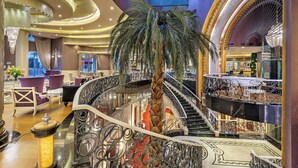 Un hall d’entrée luxueux, agrémenté d’un grand palmier au centre, d’un magnifique escalier et d’un espace détente avec des fauteuils violets.