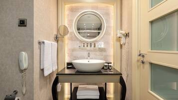 A bathroom with a round mirror, a white sink, a towel rack, a telephone, and a glass-enclosed door.