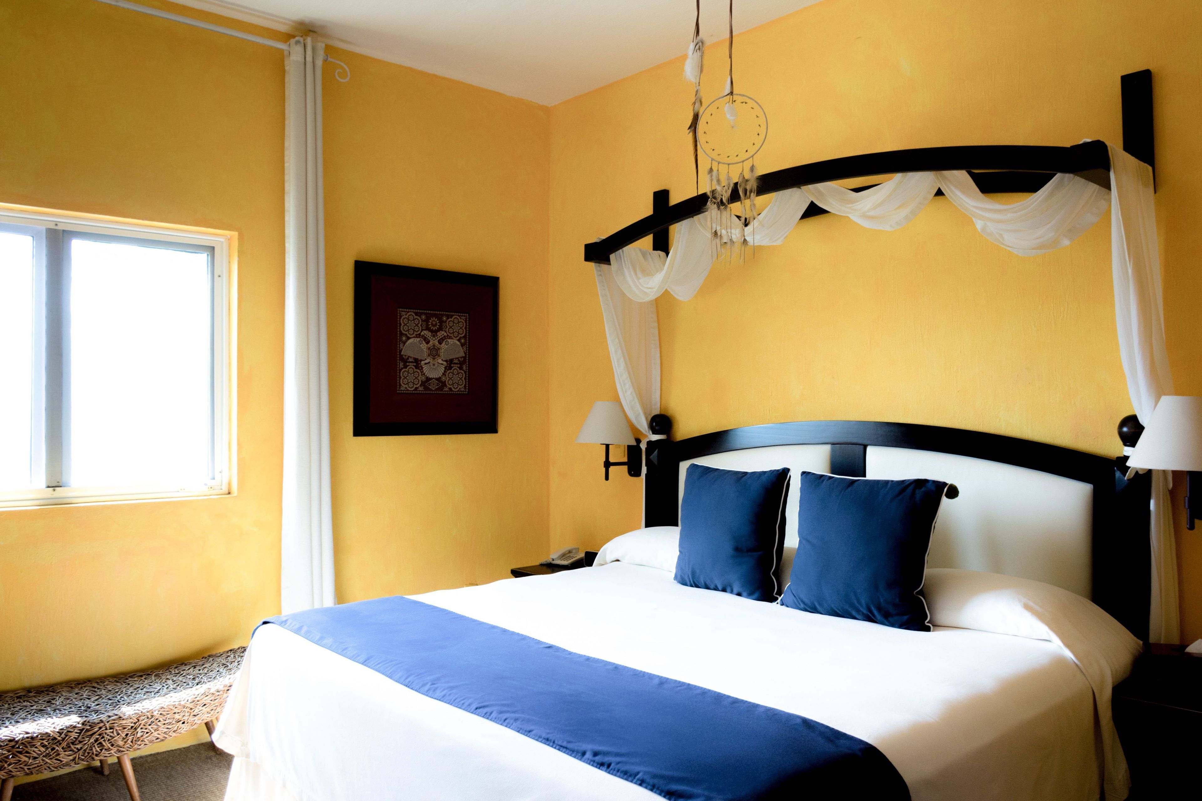 Habitació d'hotel amb llit, una panxa, una làmpada penjada a la paret i una fotografia emmarcada.