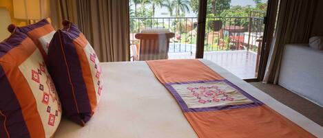 A hotel room with a bed, a view of the outdoors, and a balcony with a pool.