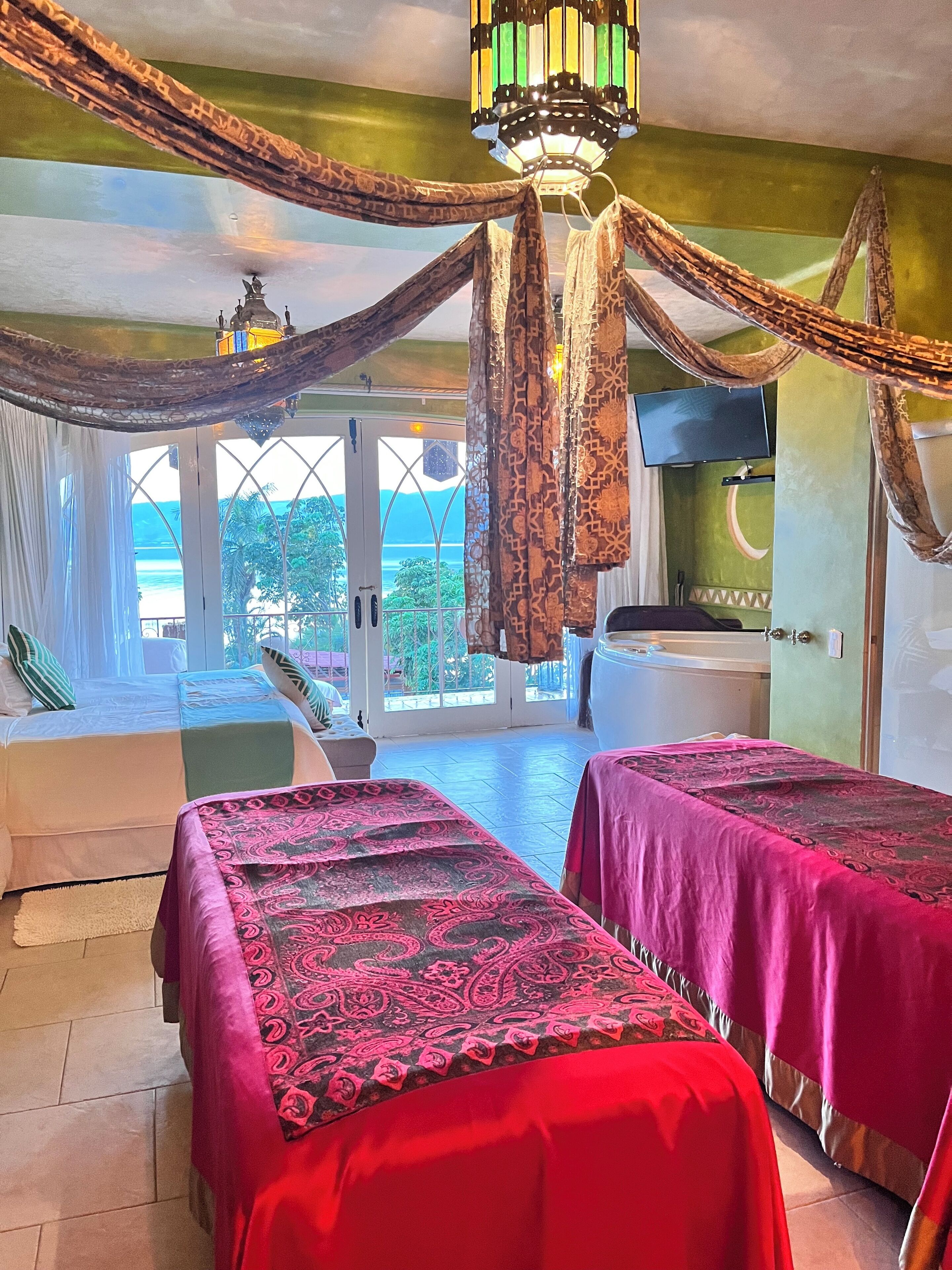 A room with two beds, a TV, a bathtub, and a view of the sea.