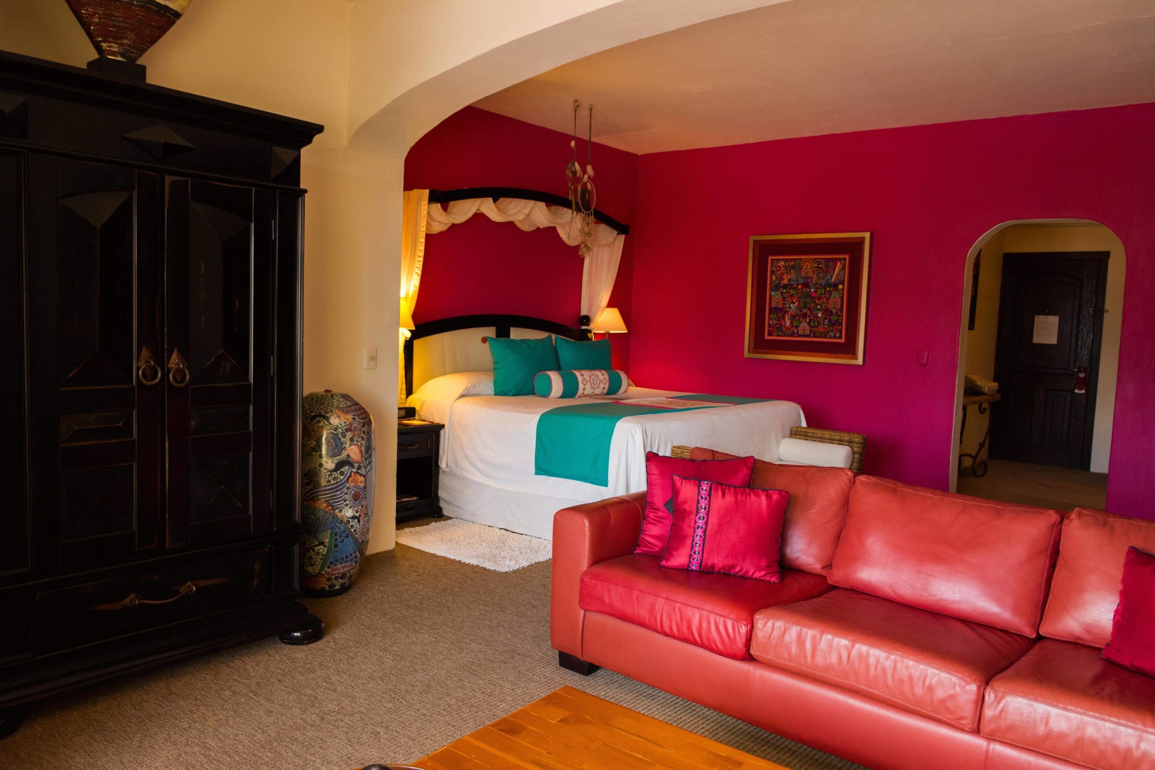 A bedroom with a bed, a red leather sofa, a cabinet, and a colorful vase.