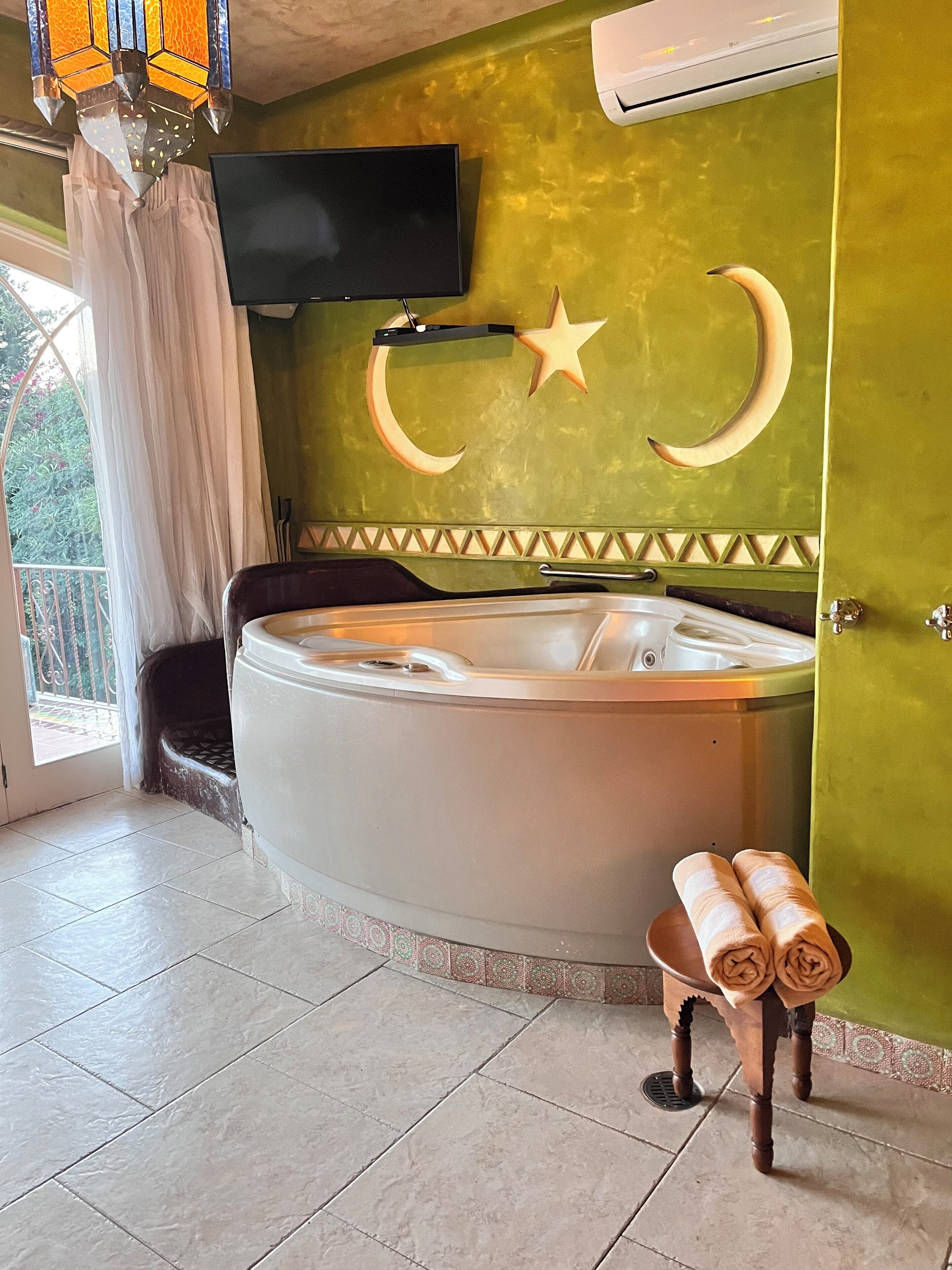Un baño con una bañera grande, un televisor montado en la pared y una decoración con forma de luna creciente.