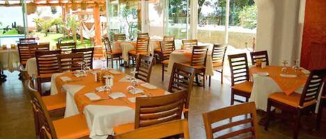A restaurant with wooden tables and chairs, covered with orange tablecloths.