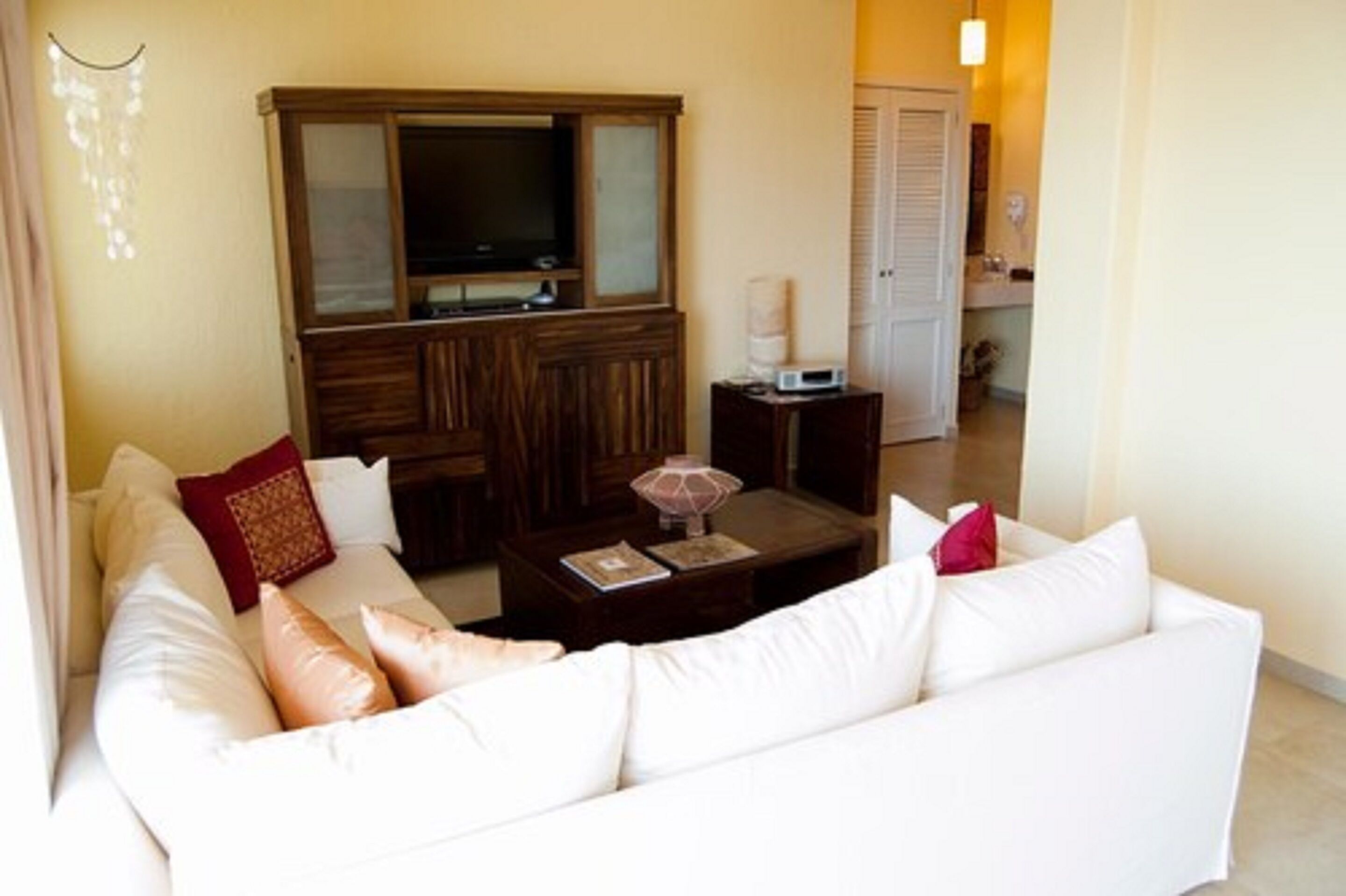 Una sala de estar con un sofá blanco, un mueble de madera, un televisor y una mesita de noche con una lámpara.