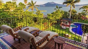 Un balcon avec deux fauteuils confortables et une petite table, donnant sur une piscine et une végétation luxuriante.