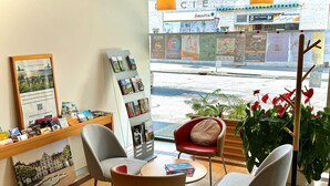 A reception area with a wooden counter displaying brochures and a framed picture, two chairs, a small table, and a view of the street outside. - ibis Delemont Delsberg Hotel (Delemont)