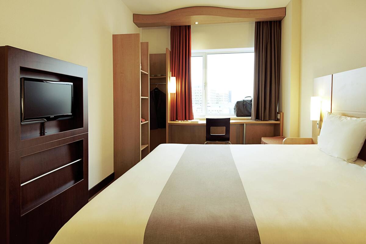 Habitació d'hotel amb llit, televisió, escriptori i armari.