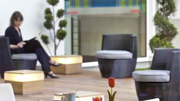 A modern hotel lobby with seating areas, a coffee table with breakfast items, and a person in the background.