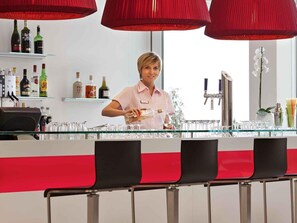 A bar area with a bartender, shelves with liquor bottles, and a red and white bar counter. - ibis Delemont Delsberg Hotel (Delemont)
