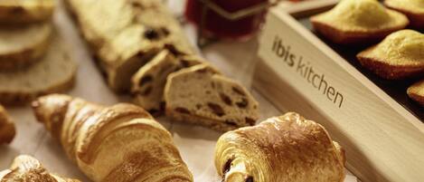A variety of pastries and bread, including croissants and a baguette, displayed on a wooden board labeled "ibis kitchen".