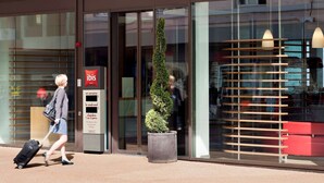 A hotel entrance with a modern design, including a glass facade, a red sign, and a potted plant. - ibis Delemont Delsberg Hotel (Delemont)