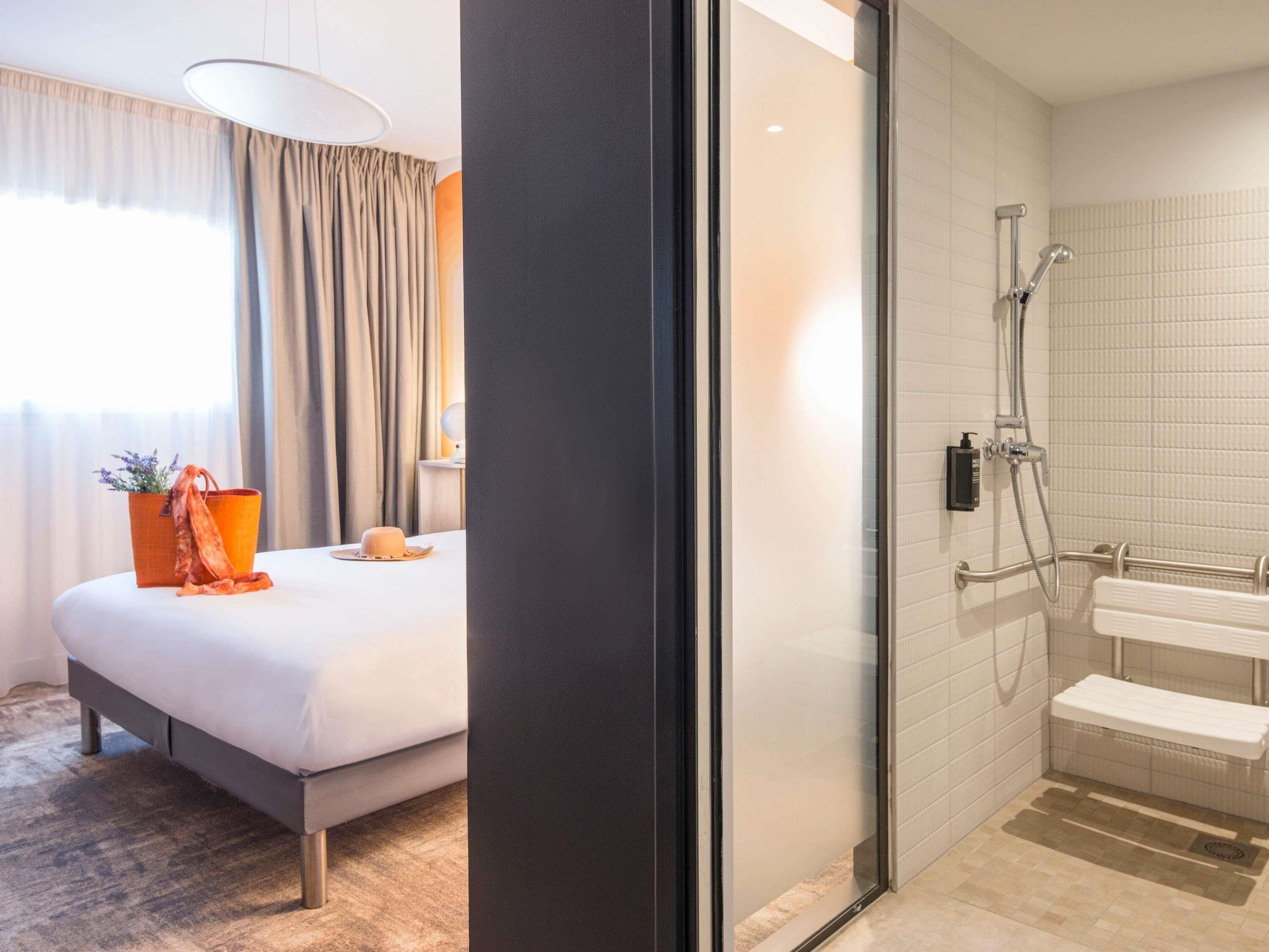 A hotel room with a bed, a bathroom with a shower, and a window with curtains.