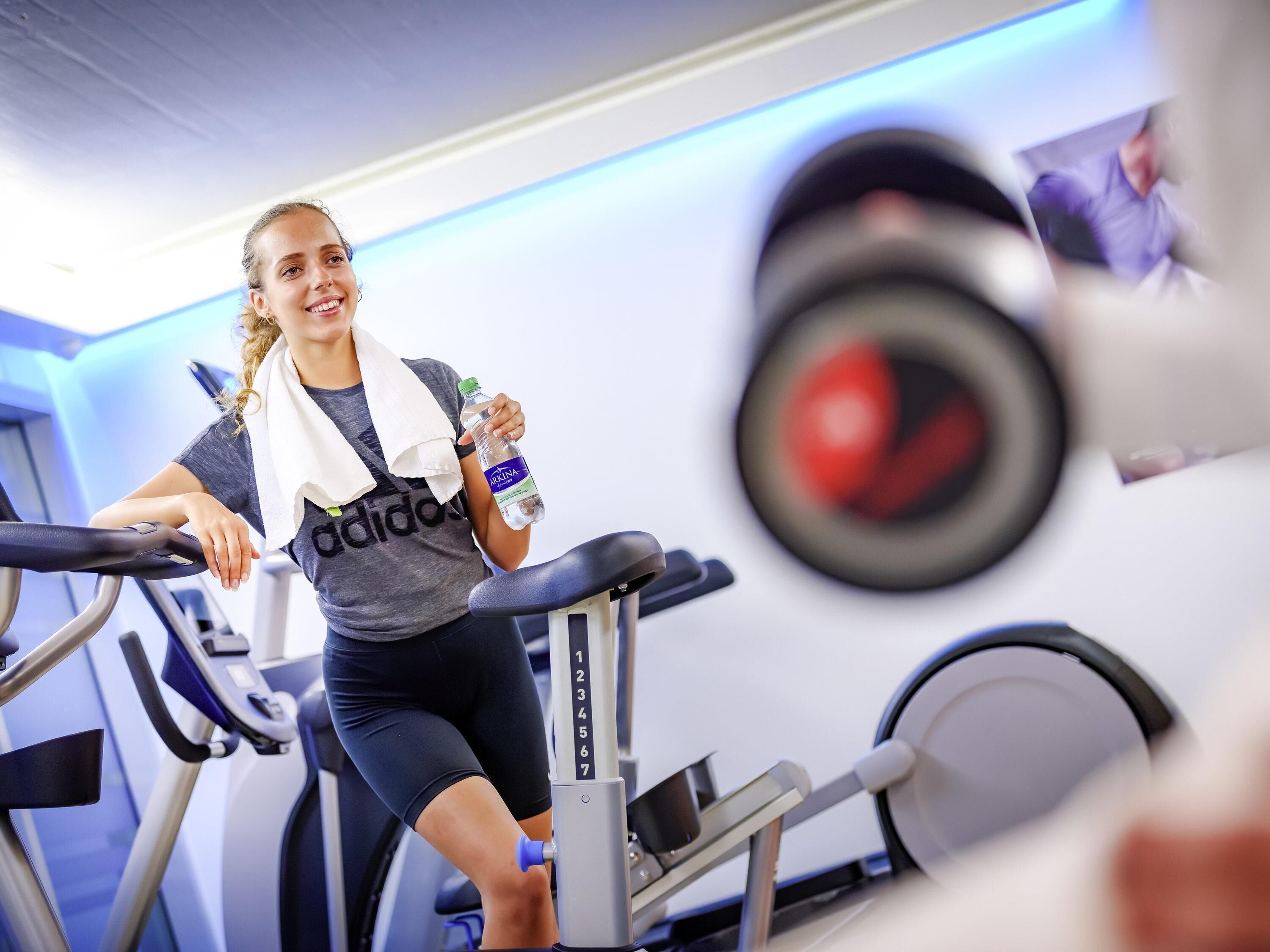 Une personne utilise un tapis de course dans une salle de sport, où l'on peut voir des poids et une bouteille d'eau.
