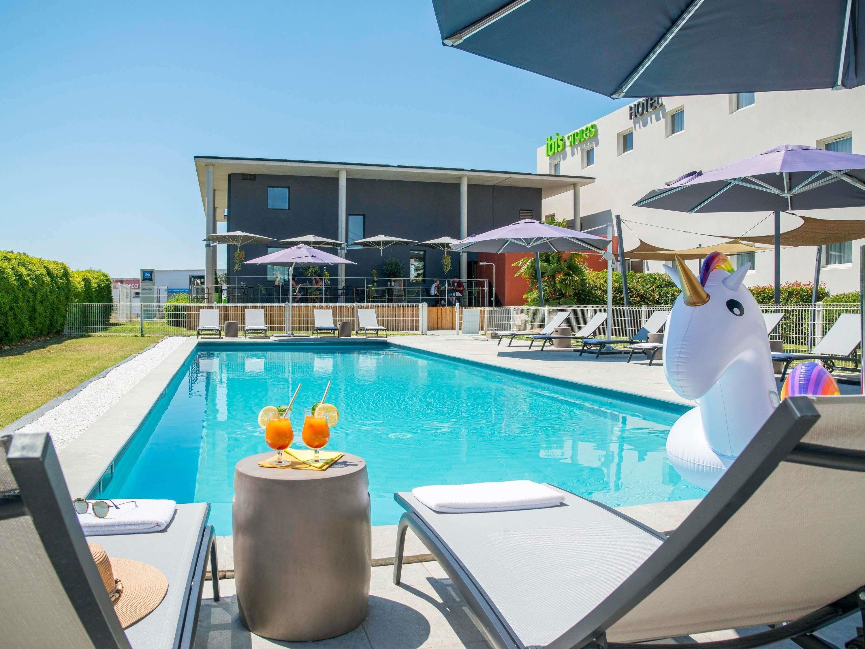 Uma piscina com espreguiçadeiras e guarda-sóis, uma decoração de unicórnio branco, e um edifício com uma placa que diz 'bis hotel'.