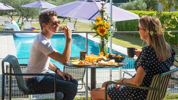 A poolside dining area with a table set for two, surrounded by umbrellas, and a pool in the background.