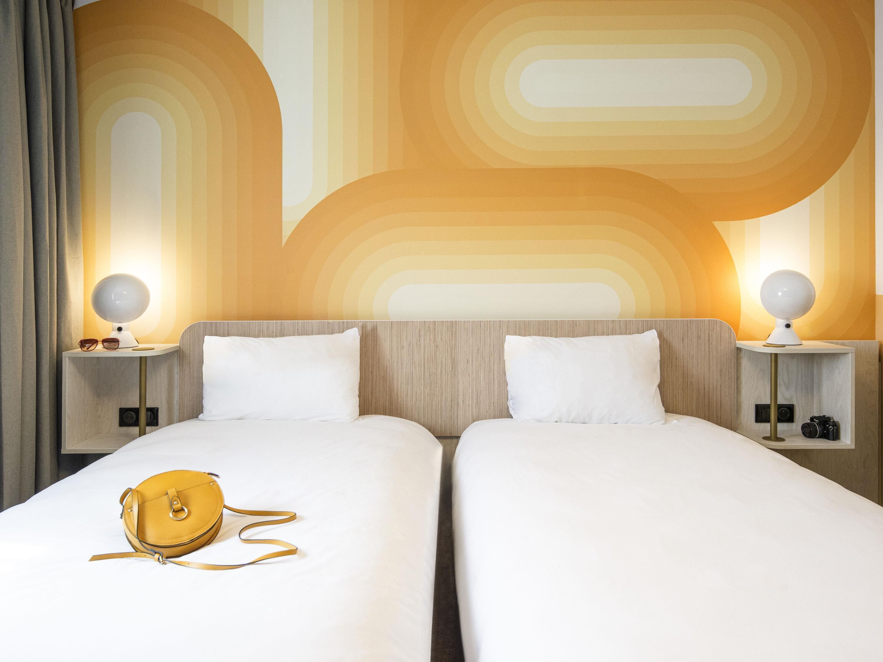 A hotel room with two beds, a lamp, a camera, and a handbag on the bed.