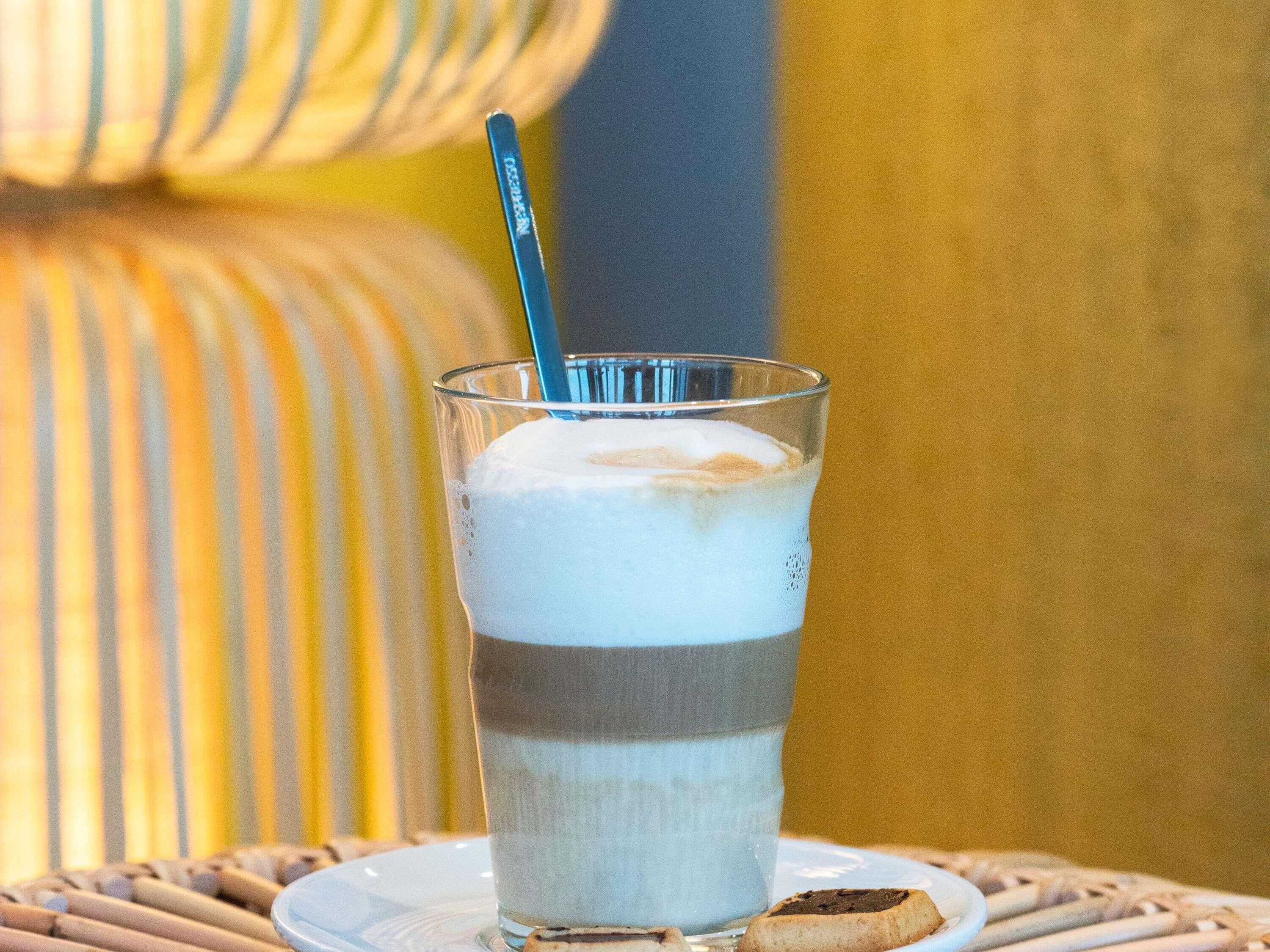 Un vaso con una bebida en capas, una pajita, una galleta y un cojín a rayas al fondo.