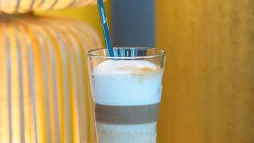 Un vaso con una bebida en capas, una pajita, una galleta y un cojín a rayas al fondo.