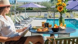 A person reading a book at a poolside table with food and drinks, surrounded by lounge chairs and umbrellas. - ibis Styles Pertuis Luberon (Pertuis)