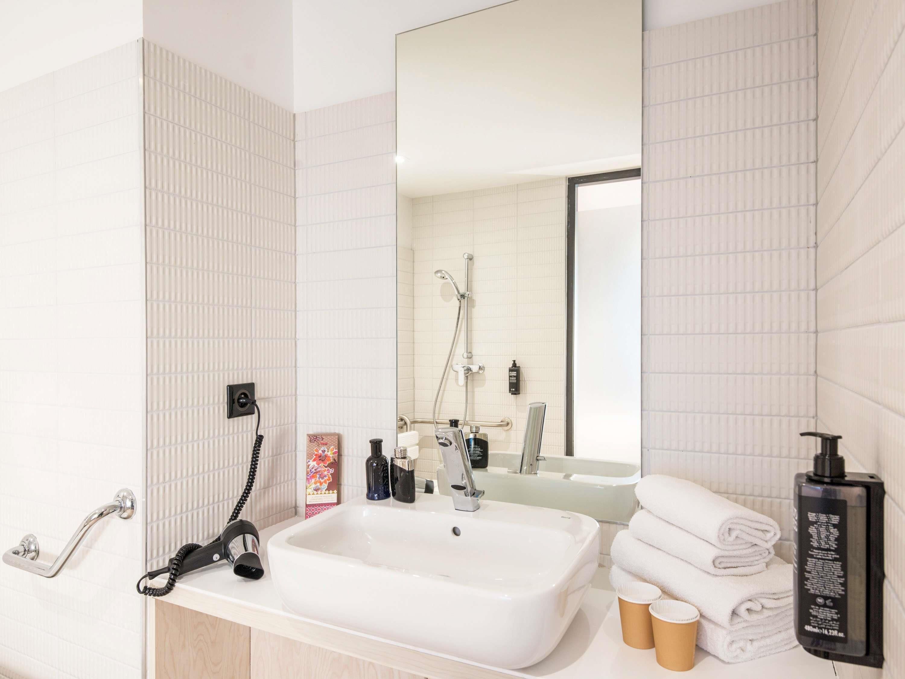 A modern bathroom with a white sink, a handheld showerhead, a towel rack, and a mirror.