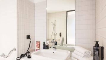 A modern bathroom with a white sink, a handheld showerhead, a towel rack, and a mirror.