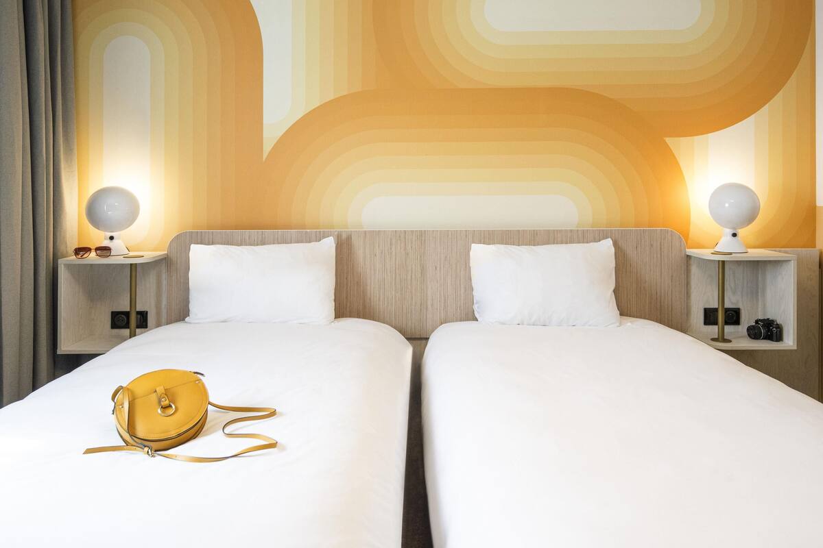 A hotel room with two beds, a lamp, a camera, and a handbag on the bed.