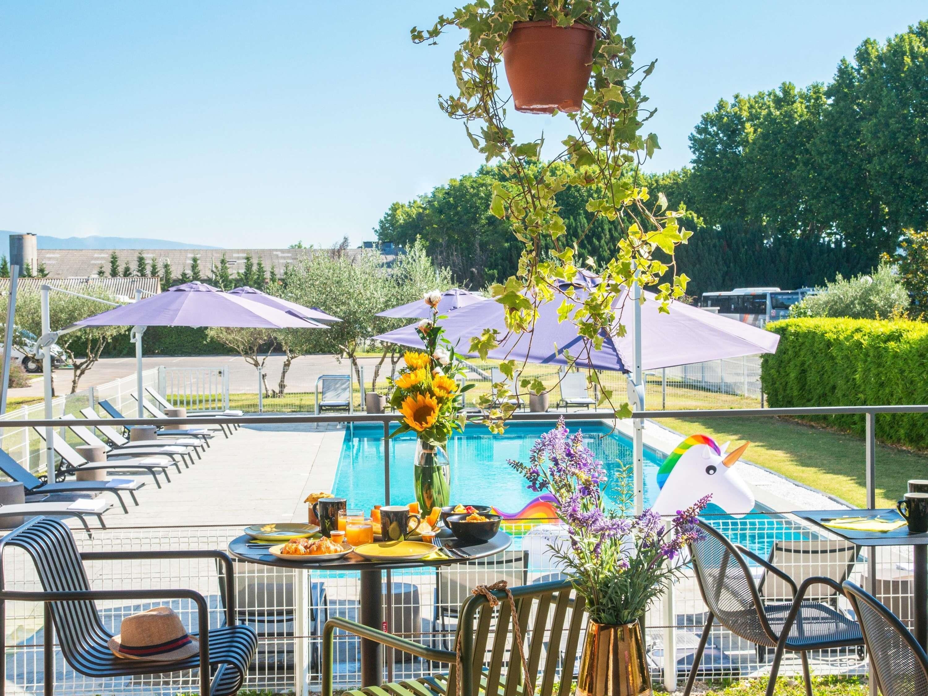 Zona junto a la piscina con una mesa dispuesta para el desayuno, girasoles y flores moradas.