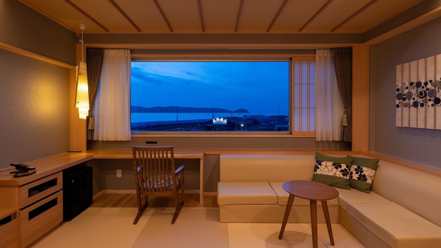 A room with a large window, a desk, a chair, a sofa, and a small table.