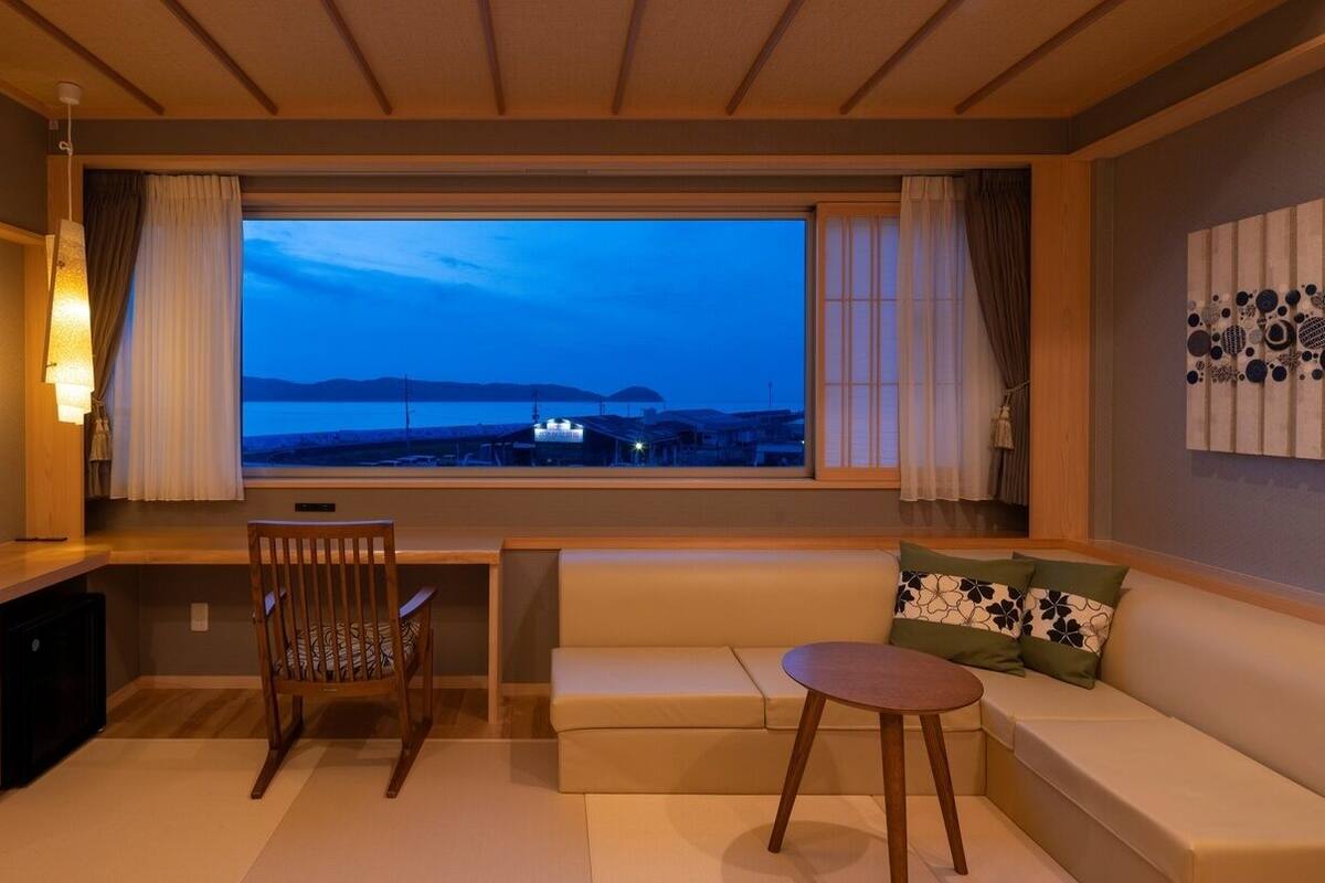 Ein Zimmer mit großem Fenster, Schreibtisch, Stuhl, Sofa und kleinem Tisch.