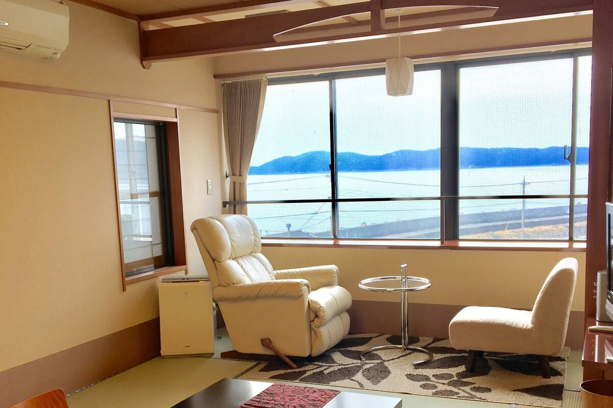 Ein Zimmer mit Esstisch, zwei Stühlen, einer Couch, einem kleinen runden Tisch und Meerblick.