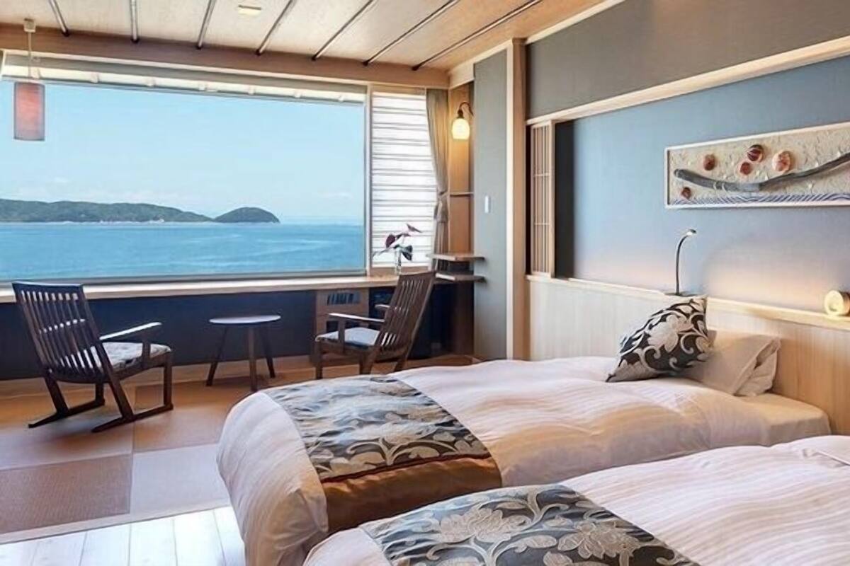 Ein Zimmer mit zwei Betten, einem Schreibtisch und einem Stuhl, mit Blick auf das Meer.