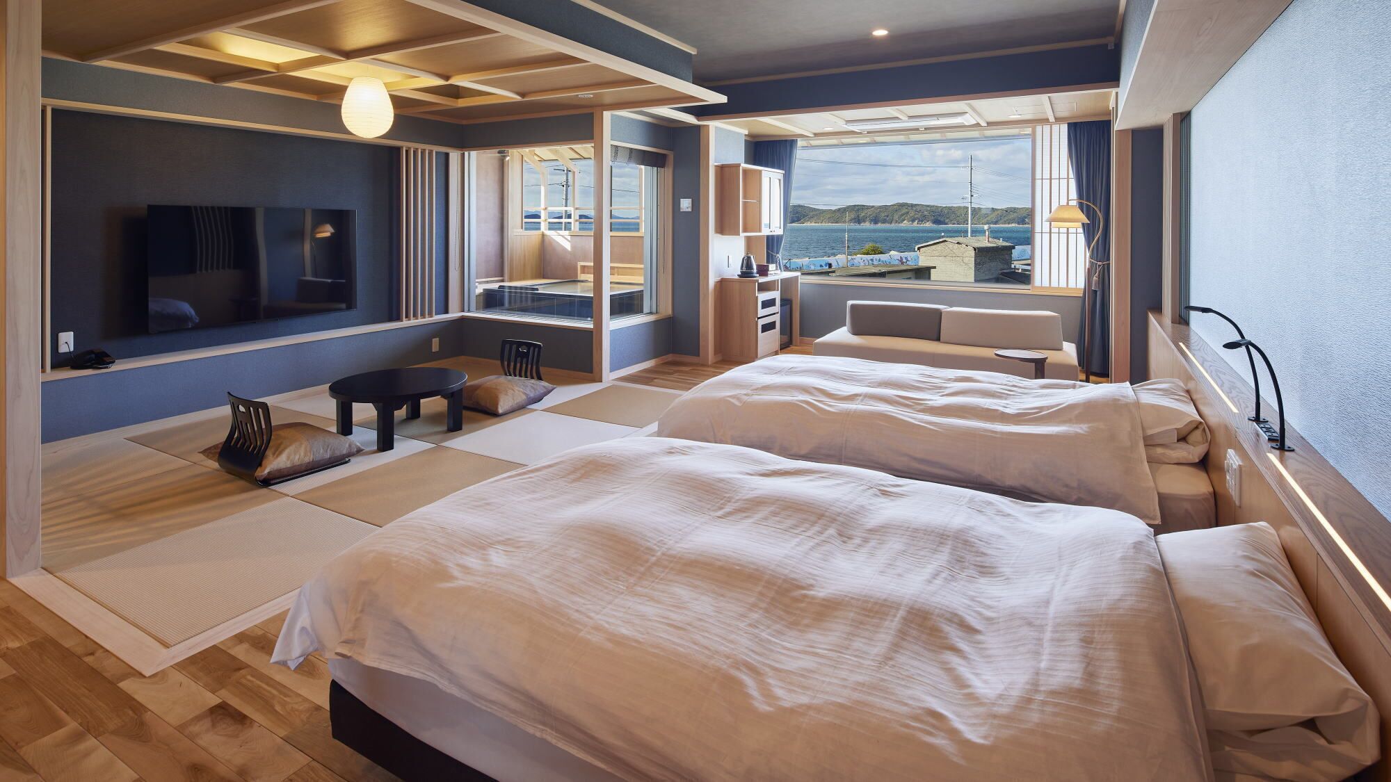 Una habitación de hotel moderna con dos camas, televisión, escritorio y vista al mar.