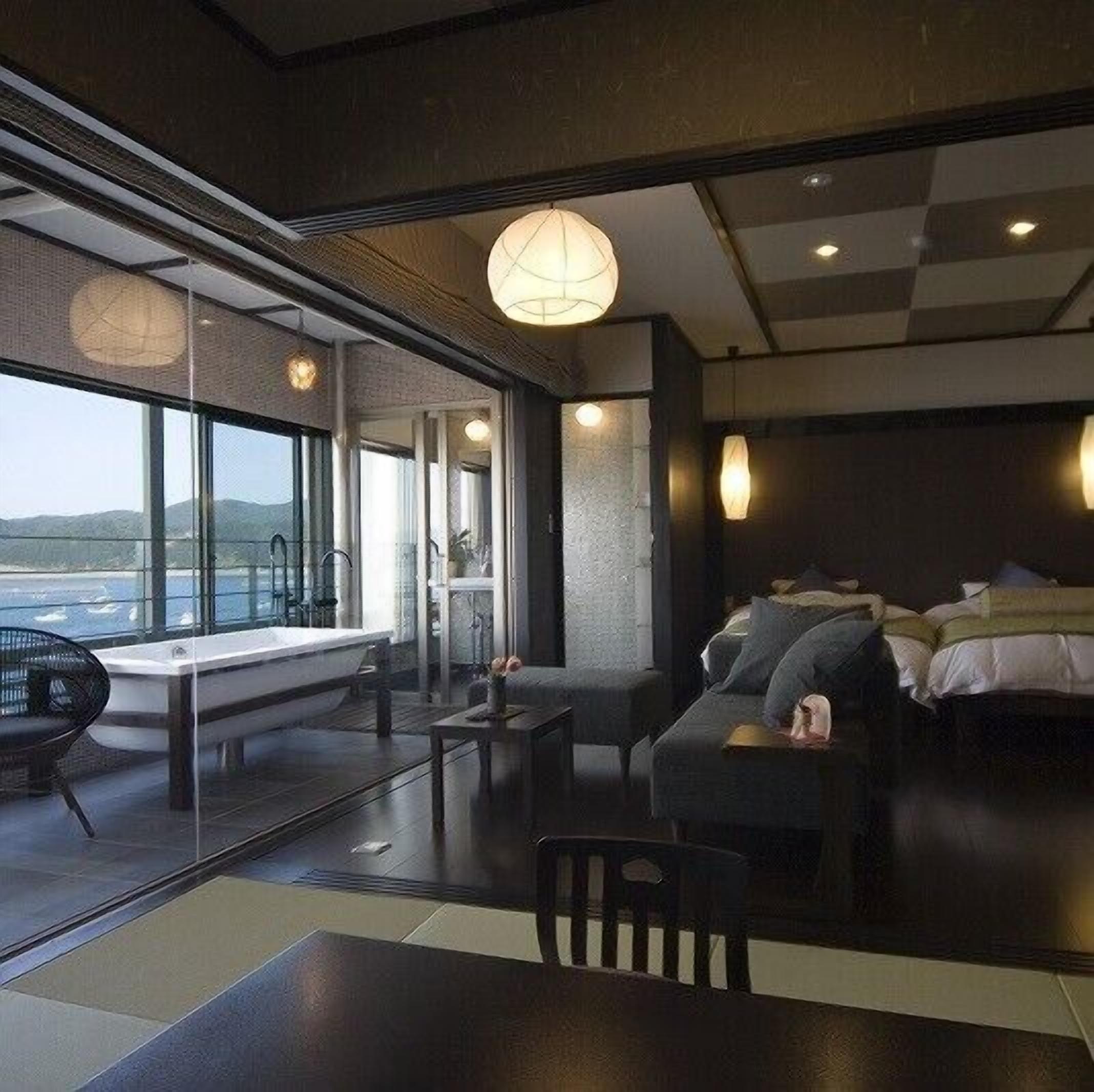 A modern hotel room with a large window, a sofa, a table, and a bed.