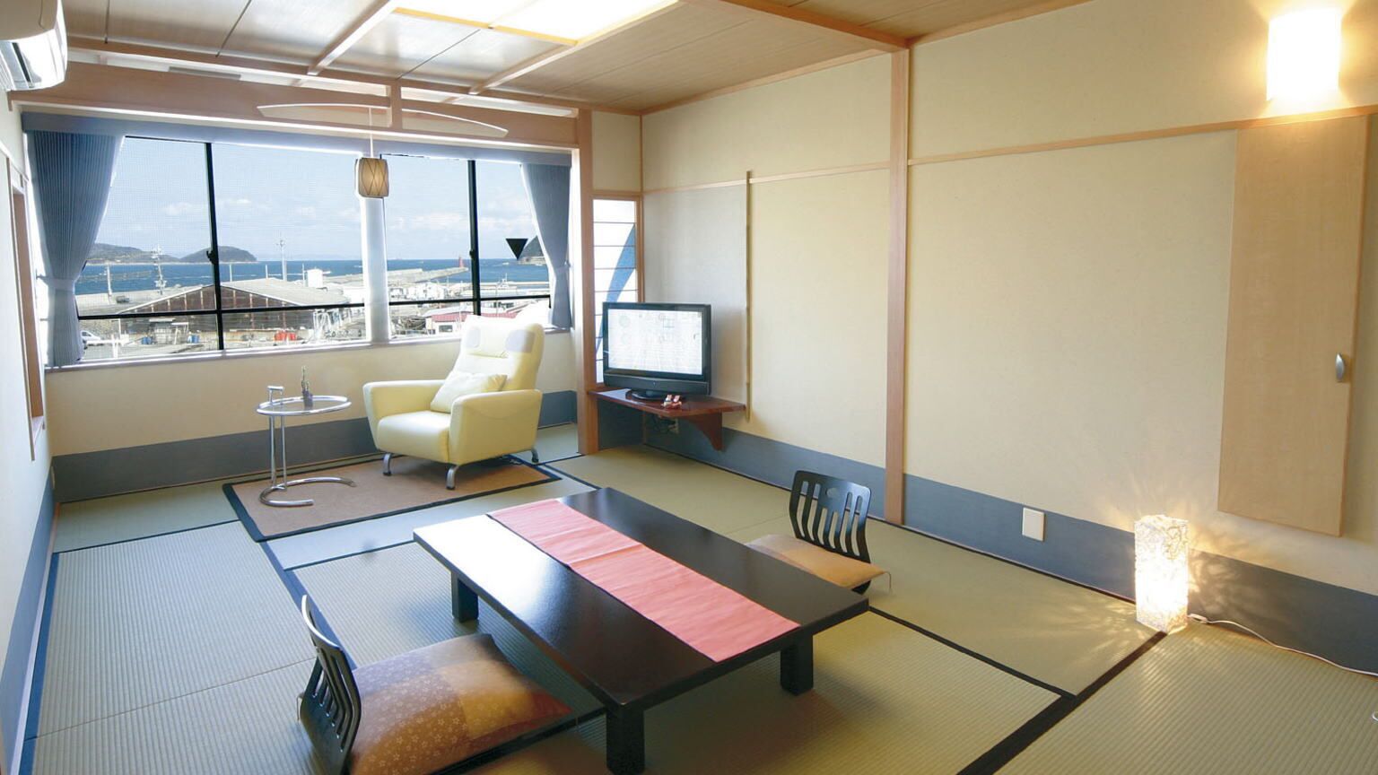 Una habitación de estilo japonés tradicional con suelo de tatami, una mesa baja, un sofá, un televisor y vistas al mar y al aeropuerto.