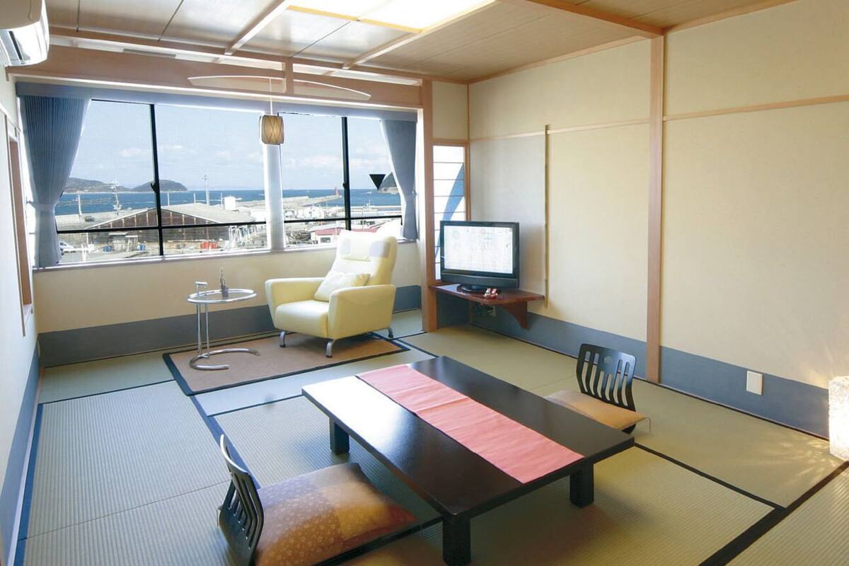 Ein traditionell japanisch gestalteter Raum mit Tatami-Boden, einem niedrigen Tisch, einer Couch, einem Fernseher und Blick auf das Meer und den Flughafen.