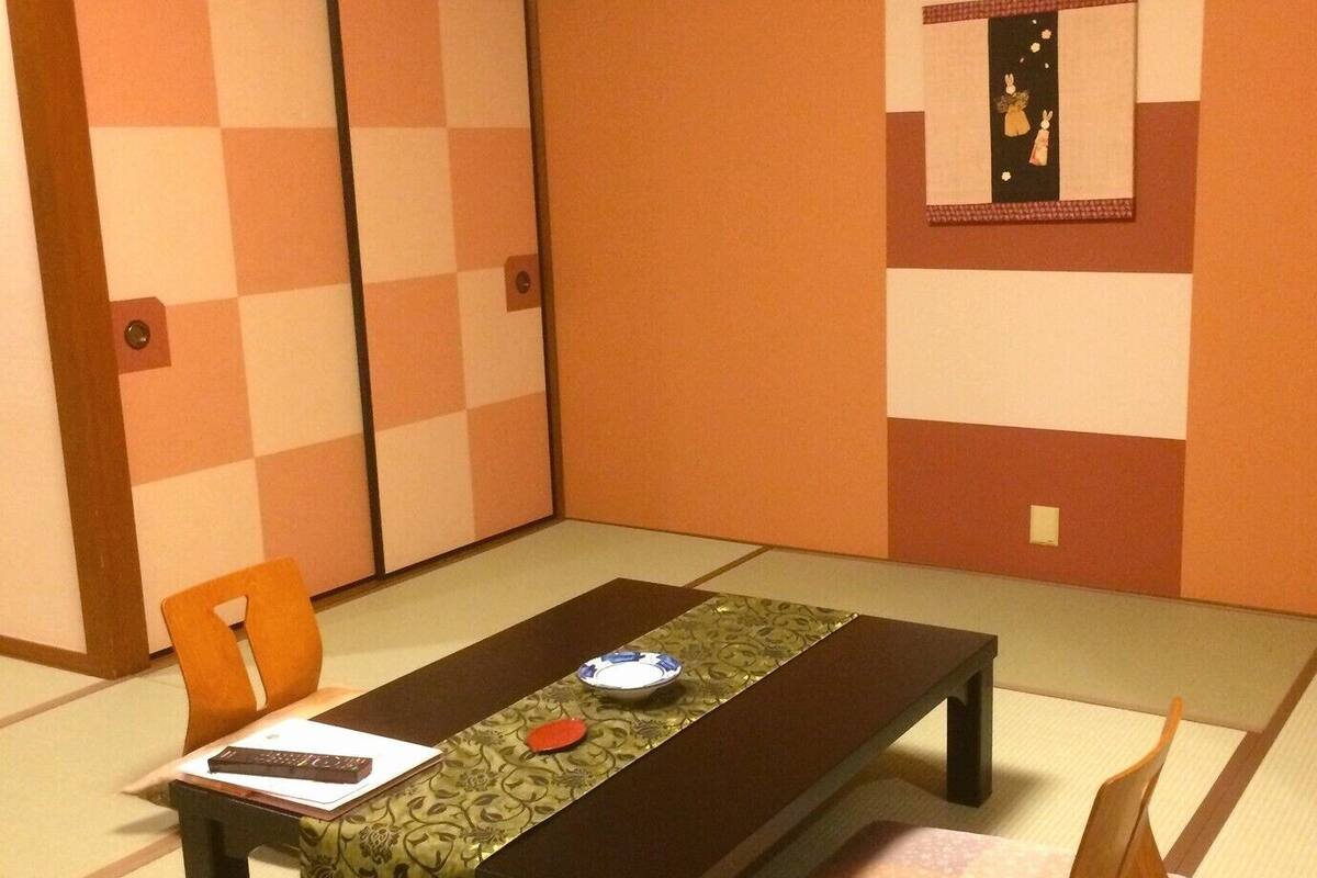 Ein traditioneller Raum mit Tatami-Matten, einem niedrigen Tisch, Stühlen und einem dekorativen Kissen.