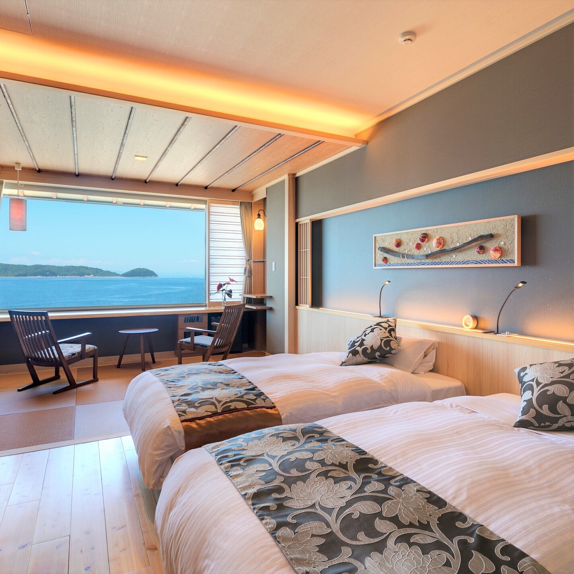 A bedroom with two beds, a desk, and a view of the sea.