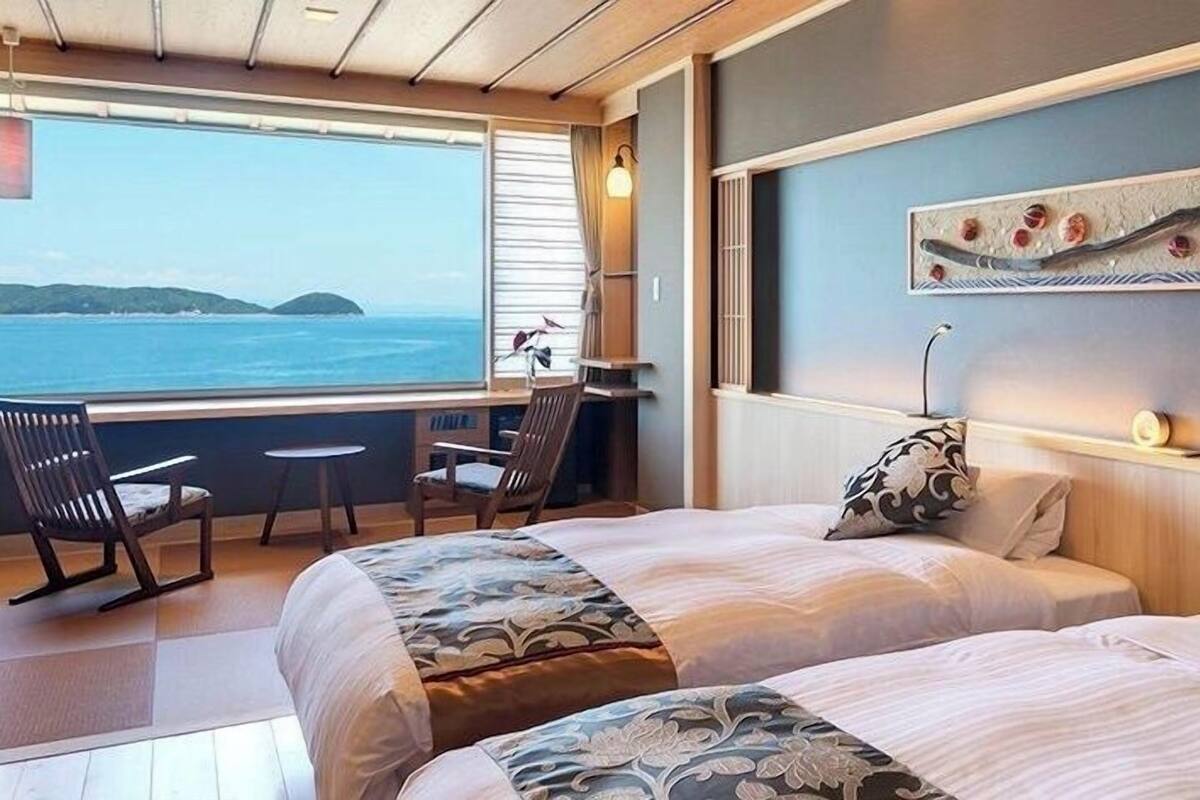 Ein Zimmer mit zwei Betten, einem Schreibtisch und einem Stuhl, mit Blick auf das Meer und die Hügel.