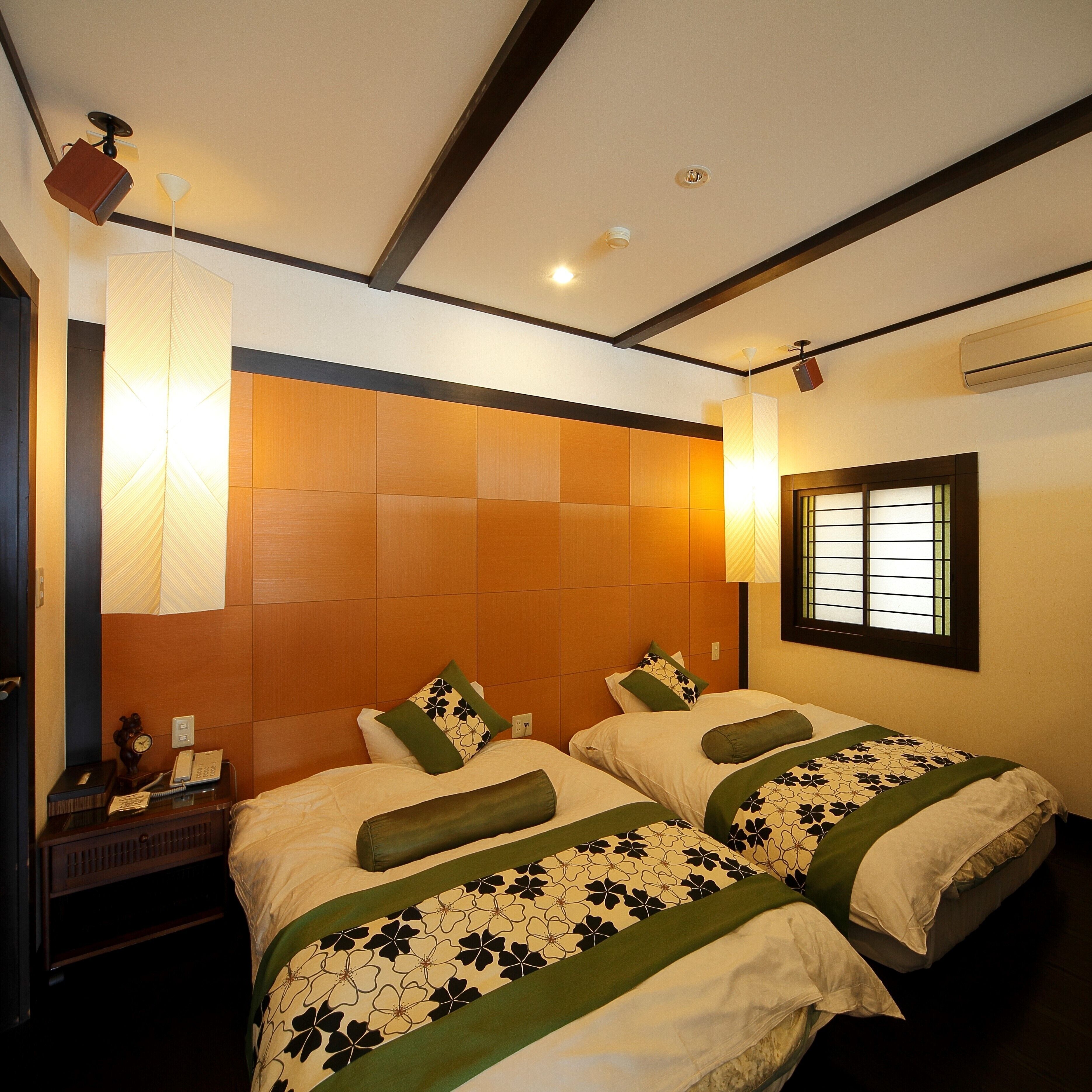 A hotel room with two beds, a nightstand, a clock, a telephone, and a window with blinds.
