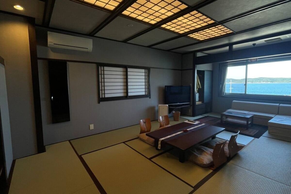 Ein Zimmer mit Tatami-Boden, einem Fernseher, einer Couch und Meerblick.