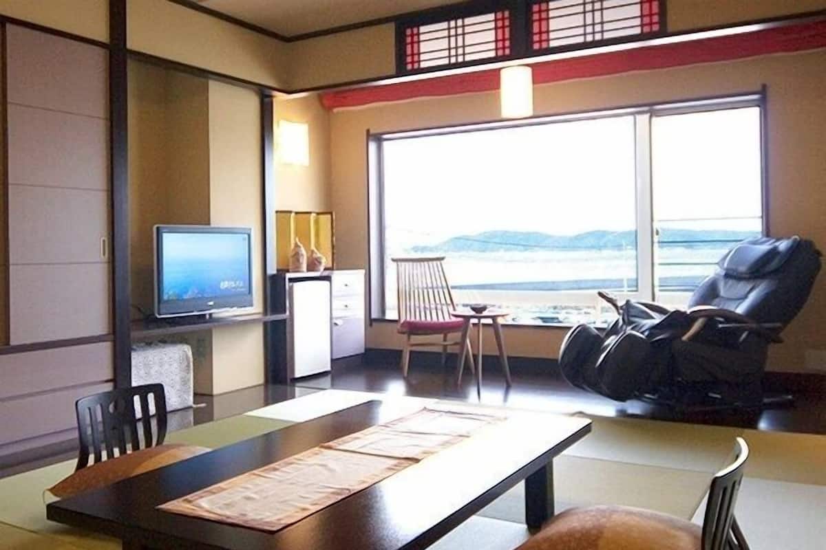 Ein Zimmer mit Fernseher, Massagesessel, Esstisch und Meerblick.