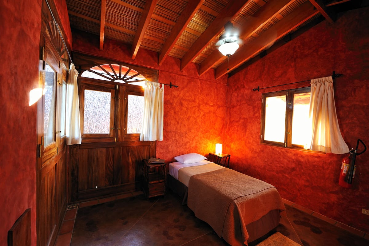 A room with a bed, a nightstand, a wooden wardrobe, and a window with curtains.