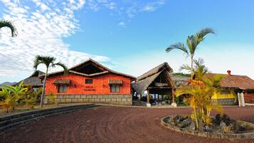 A traditional building with a thatched roof and a red exterior, surrounded by a landscaped area with palm trees.