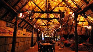 An indoor space with a high thatched roof, stone walls, and a central seating area with tables and chairs. - Hacienda Puerta Del Cielo Ecolodge & Spa (Nandasmo)