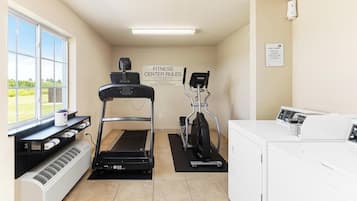 A fitness center with a treadmill, elliptical, and stationary bike, a washer and dryer, and a sign with fitness center rules.